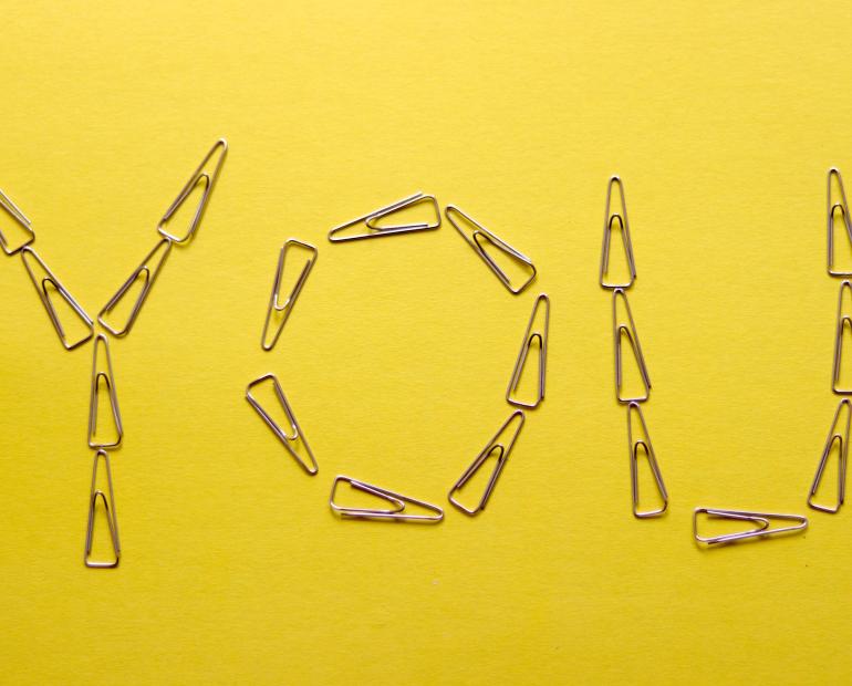 Paper clips position to spell out "You" on a yellow paper.